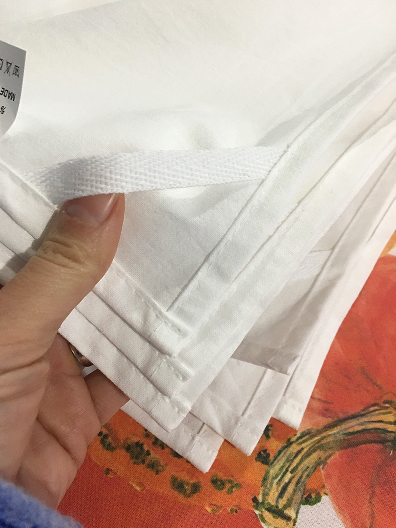 A stack of tea towels. Only the underside of the corner is shown with the hang tag sewn into it.